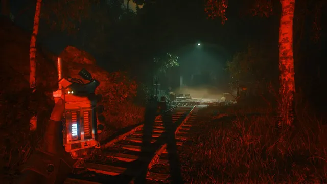 Night on overgrown railway tracks bathed in red light, the handheld noise meter in the foreground