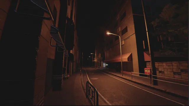 An empty town street at night lined with apartment blocks, shop awnings and a red post box