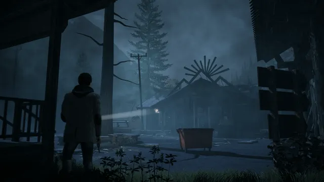 Alan Wake Remastered screenshot: Alan points a flashlight across a dark, misty forecourt at an abandoned diner with a sunburst sign