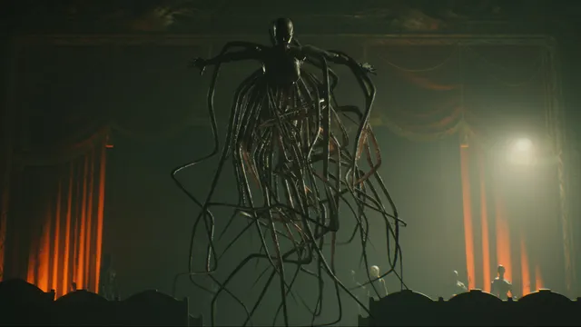 A towering creature of black cables hanging above a theatre stage lit by a spotlight