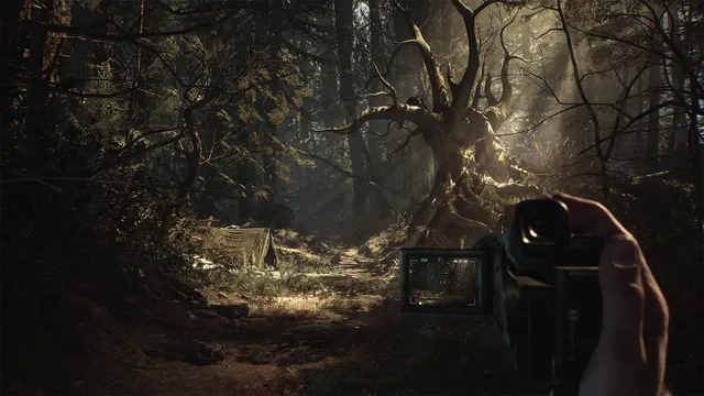 Blair Witch screenshot: a first-person hand holds an old camcorder showing the forest on its flip screen, before a gnarled tree and an abandoned tent