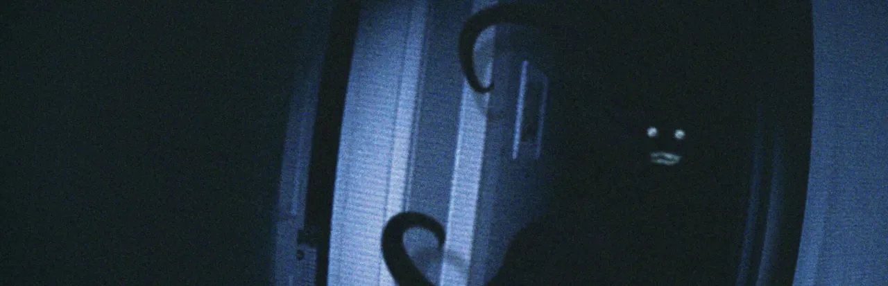 CAPTURED key art: a dark figure with small white eyes and a grin peers around a doorway, with tentacles curling in the grainy camcorder light