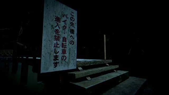 A weathered Japanese sign at the steps to a bridge at night, banning bikes and bicycles