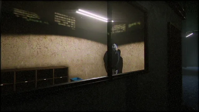 Through a window, a dark figure stands with its back turned in a bare lit room of the apartment