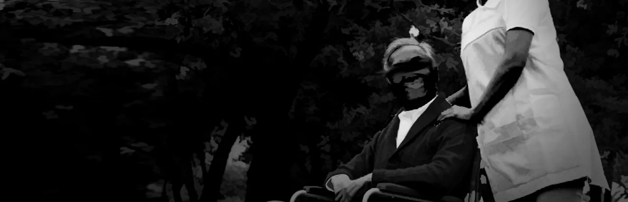 The Caregiver key art in black and white: a caregiver in a white uniform with her hands on the shoulders of an old man in a wheelchair, both faces blacked out