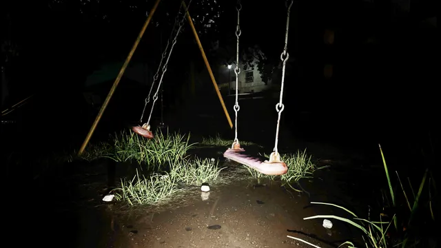 Swings over wet grass at night, lit by a flashlight