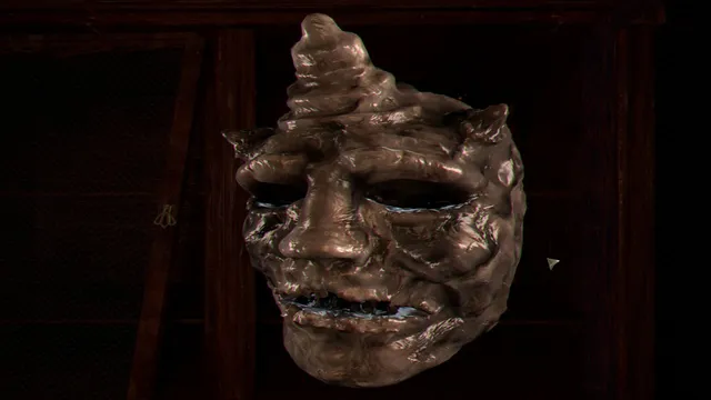 A grotesque bronze mask with a twisted horn and empty eyes hanging on a dark wall