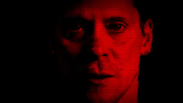 A man's face in close-up, lit deep red, as on a corrupted video frame
