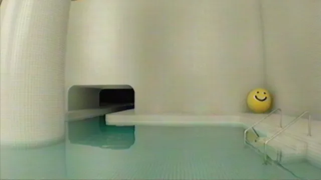 A white tiled pool room with a tunnel opening and a yellow smiley-face ball by the steps