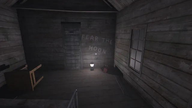 Fear the Moon screenshot: inside a bare wooden cabin, the words Fear the Moon are scrawled on the wall beside the door, lit by a lantern on the floor
