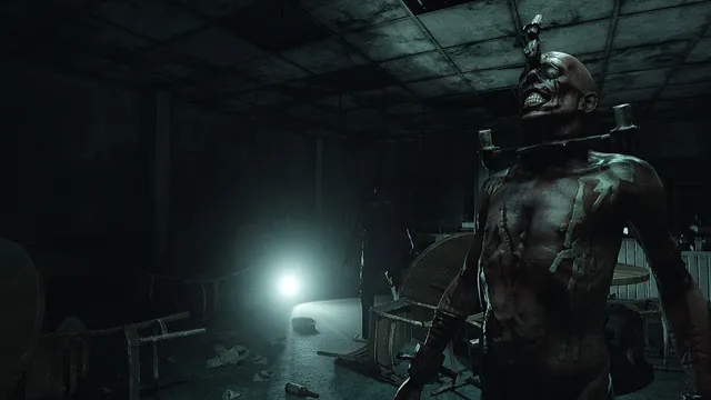 Fear The Timeloop screenshot: a grinning, stitched-up man held upright by a metal brace in a dark, wrecked room lit by a single torch
