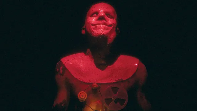 A red-lit creature with a stretched grinning face and a reel device strapped to its chest
