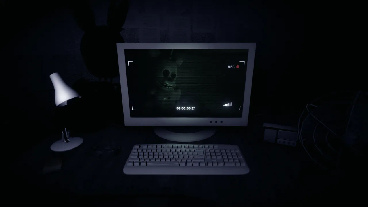 An old security office at night: a desk lamp, keyboard and computer monitor showing a camera feed of a withered rabbit animatronic
