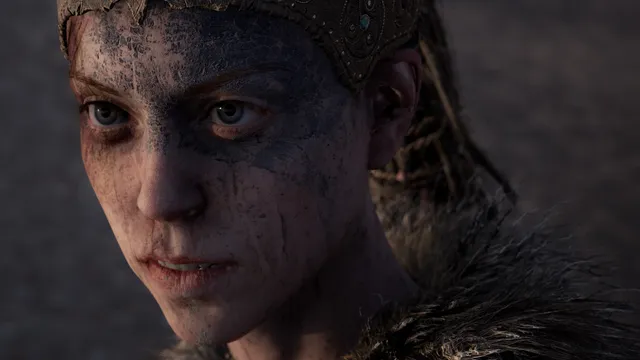 Hellblade: Senua's Sacrifice screenshot: a close-up of Senua's face, smeared with dark paint and dirt, beneath a beaded headband
