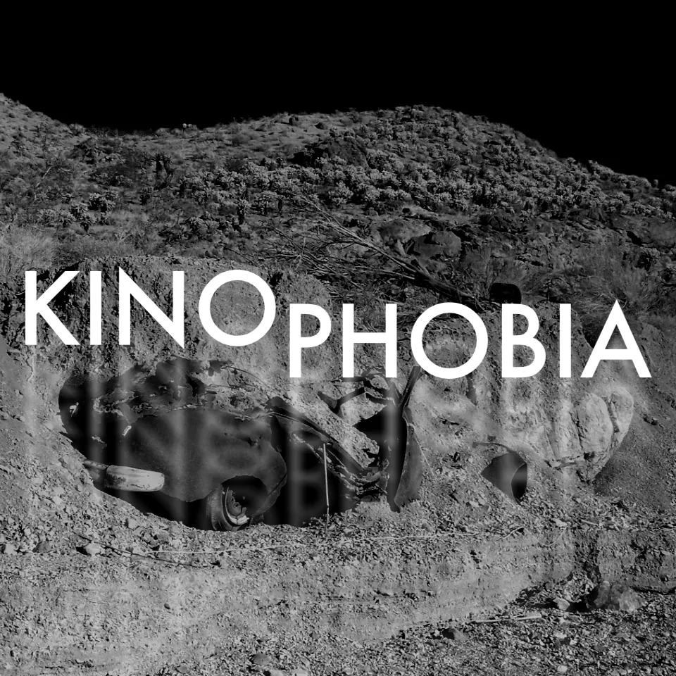 Kinophobia cover: the title in white over a black-and-white photo of a wrecked car half-buried in a desert hillside