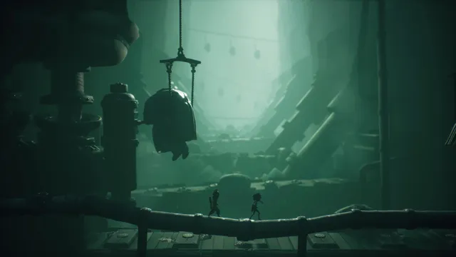 Little Nightmares III screenshot: Low and Alone cross a pipe under a hanging bell in a vast green-lit factory