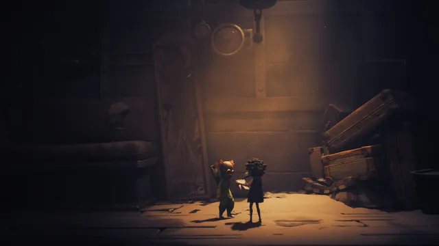 Little Nightmares III screenshot: Low and Alone stand in a dim room beside a tall door and a pile of old suitcases