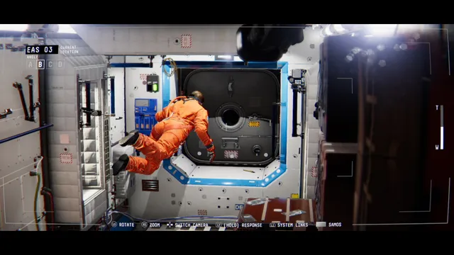 Security camera view of Emma in an orange suit floating through a white station module
