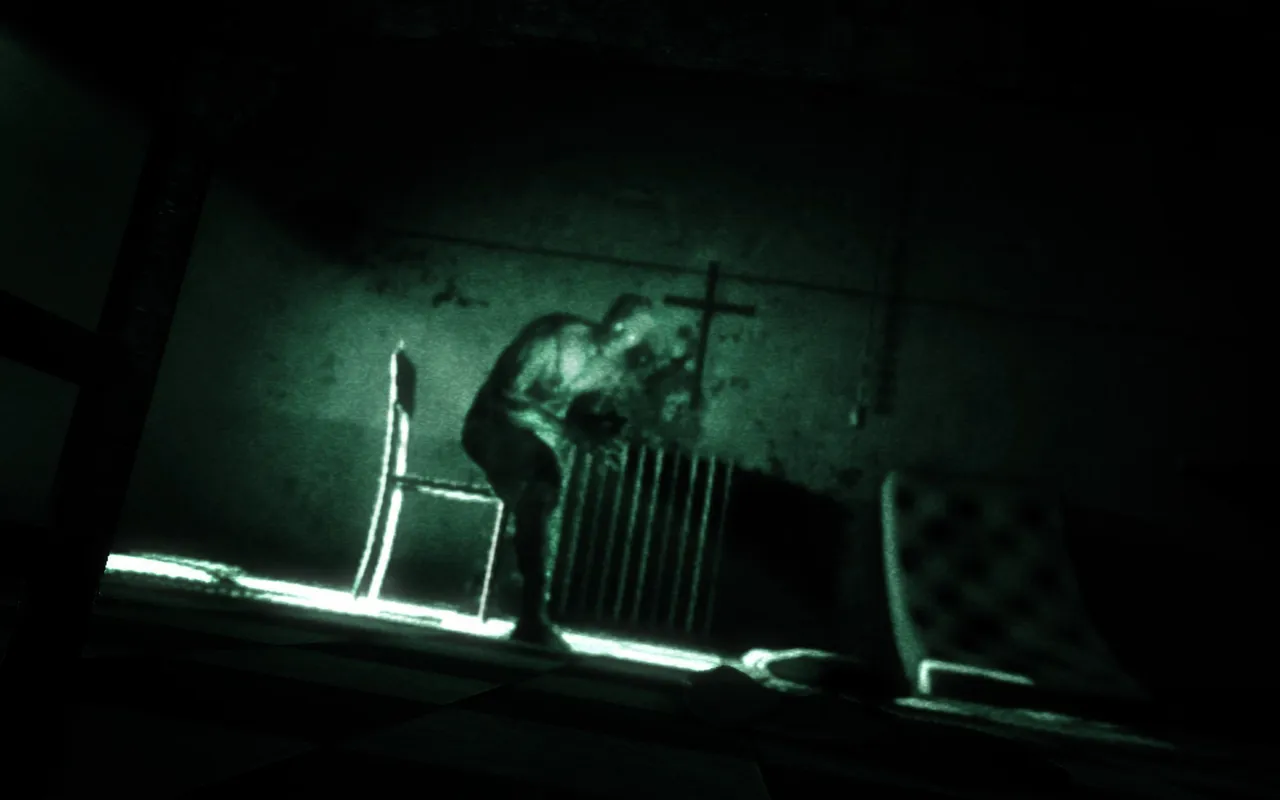 Outlast screenshot: through the camcorder's green night vision, a hunched patient crouches by a radiator in a dark room