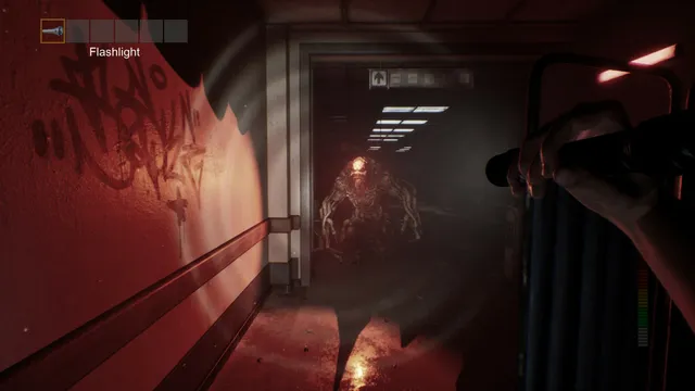 A flashlight lights a red-walled corridor with graffiti as a fleshy creature comes through a doorway