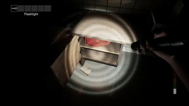 A flashlight beam picks out an open cabinet with a red item inside in a dark room
