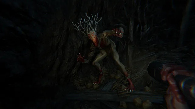 A pale, root-headed demonic creature crouching in a dark cave of roots as the player holds a flashlight