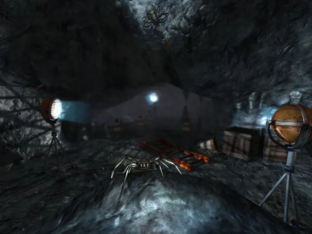 Penumbra: Overture screenshot: a large pale spider crawls across a rocky mine cavern lit by work lamps on tripods, near crates and a fallen ladder