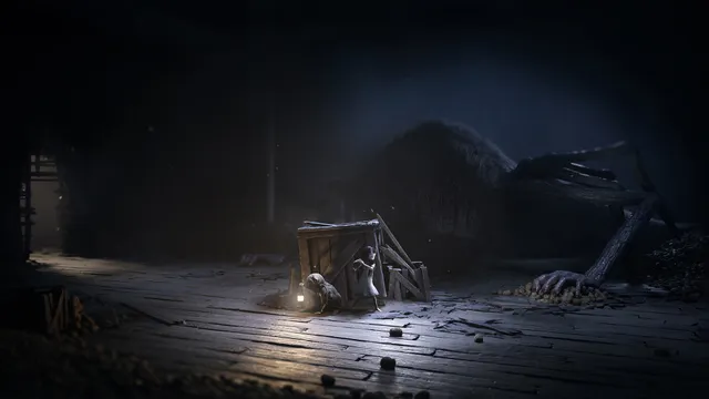 The two children crouch behind a broken crate on a wooden floor while a giant creature with long limbs lies in the dark beside them