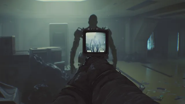 First-person view holding the C.A.T. up as its small screen shows a tall humanoid robot walking toward you through a dim room