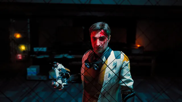 A scarred man in a white jacket holding a small mechanical device behind a wire fence