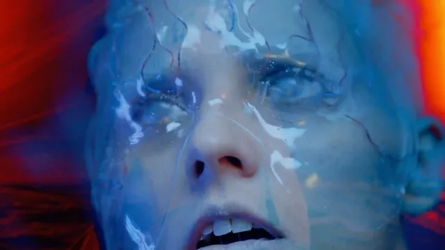 Full-motion video close-up of a woman's face under a wet, veined membrane in red and blue light