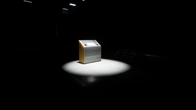 The inspection console alone in a spotlight in a pitch-dark hall