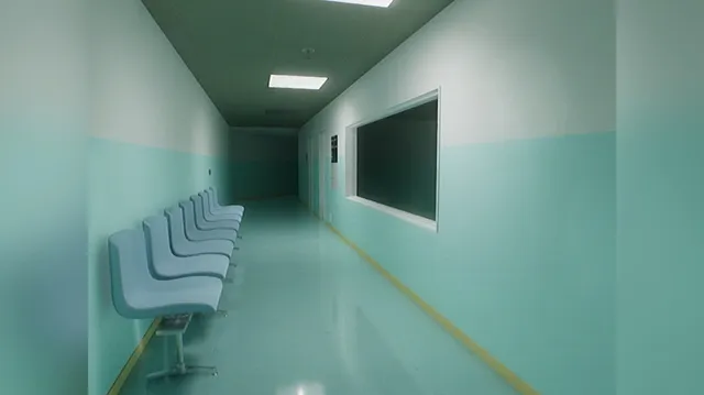 A pale green hospital corridor with a row of empty waiting chairs