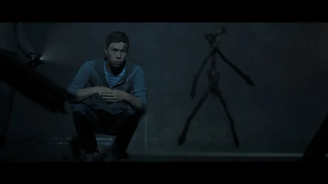 Little Hope screenshot: Andrew crouches in the dark woods beside a hanging twig effigy as a torch shines in