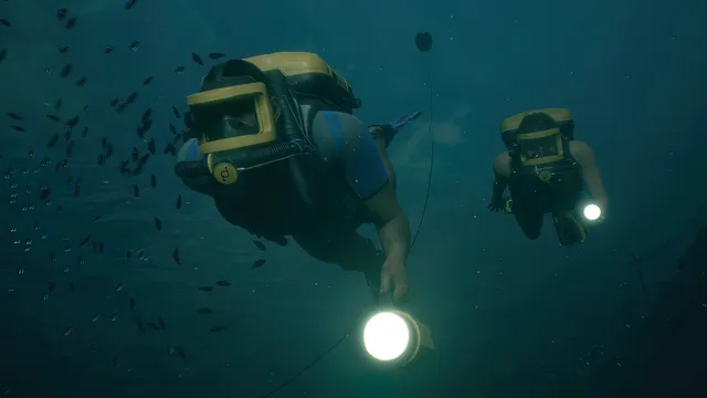 Man of Medan screenshot: two divers with torches swim through a shoal of fish in green water