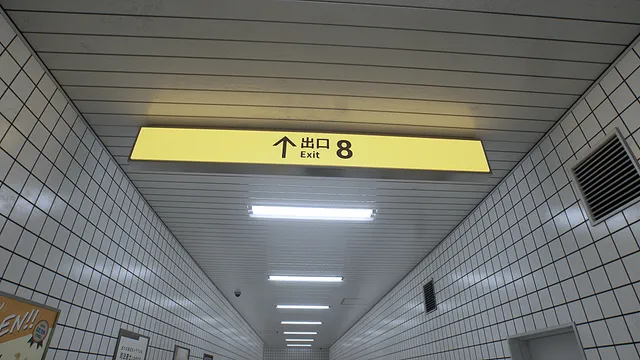 The Exit 8 screenshot: looking up at the yellow Exit 8 sign and the long row of ceiling lights in the passage