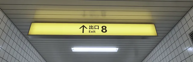 The Exit 8 key art: a yellow 'Exit 8' sign hanging from the ceiling of a white-tiled subway passage