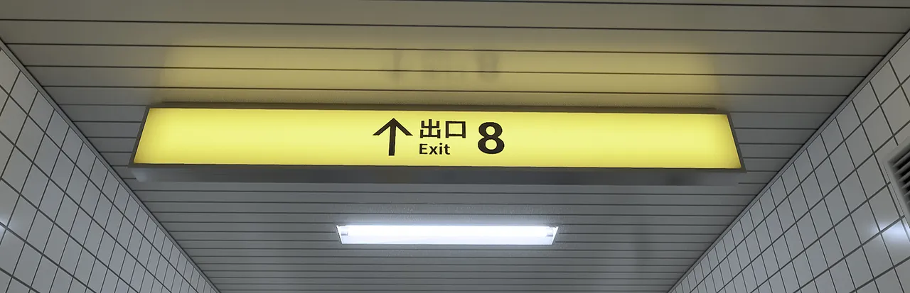 The Exit 8 key art: a yellow 'Exit 8' sign hanging from the ceiling of a white-tiled subway passage