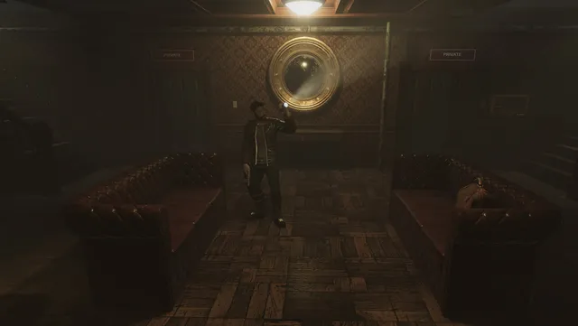 Alex stands in a dim hotel lobby between two leather sofas under a round mirror
