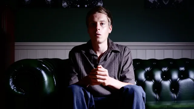 A young man leaning forward on the couch, hands clasped