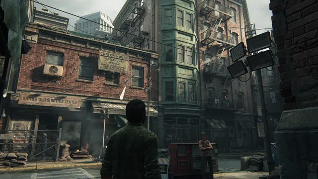 The Last of Us Part I screenshot: Joel walks a fenced-off brick street in the Boston quarantine zone past a ration distribution centre