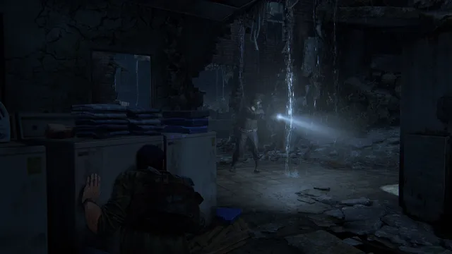 The Last of Us Part I screenshot: Joel hides behind a wall in a dark, flooded room as a figure with a flashlight searches