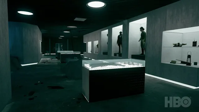 A dark exhibit hall of display cases and figures in alcoves, with dark stains on the floor
