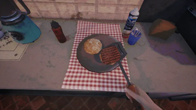 First-person view of a burger patty and a bun on a plate on a checked cloth, with a spatula in hand